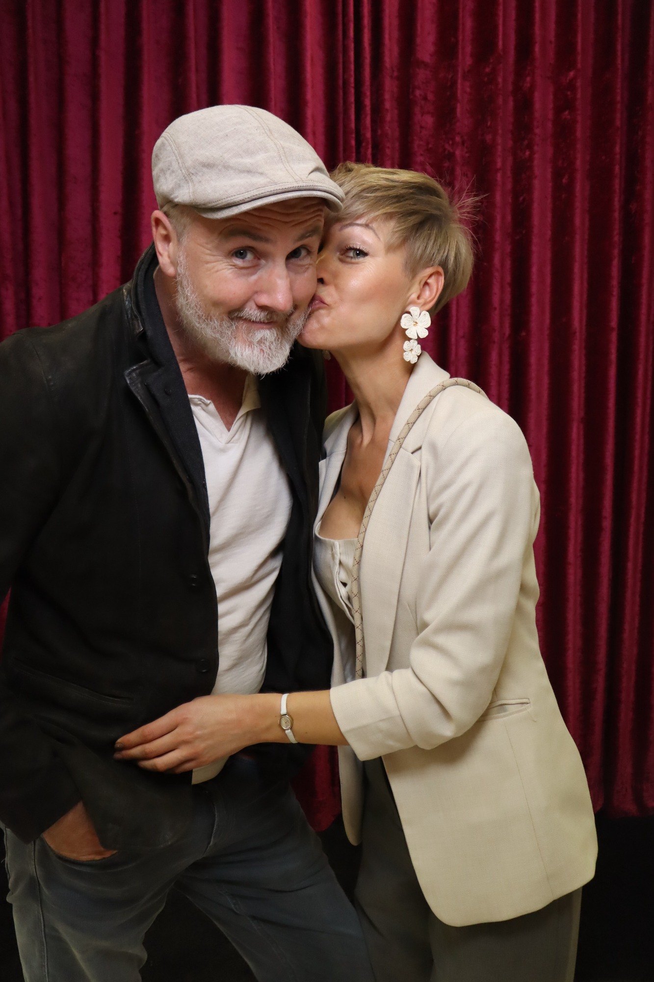 Mann mit grauem Bart und Kappe, umarmt von Frau, die ihm einen Kuss gibt.